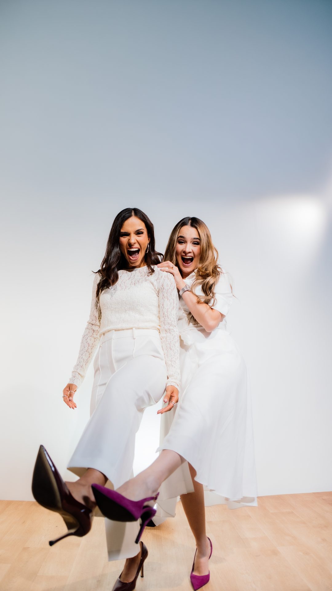 Ana Fidalgo y Michelle Ruiz, vestidas de blanco y riendo juntas en un estudio claro.