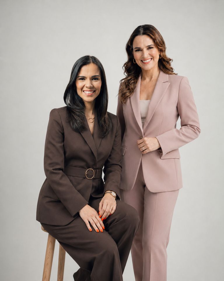 Dos mujeres en actitud de conversación, una sentada en un banco alto y otra de pie a su lado.